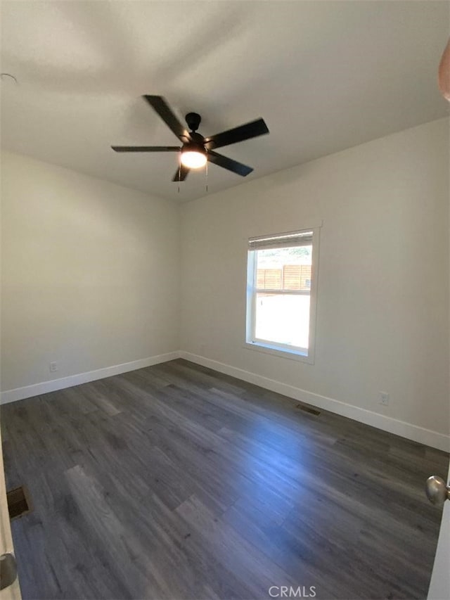 empty room with dark wood-style flooring, visible vents, baseboards, and a ceiling fan