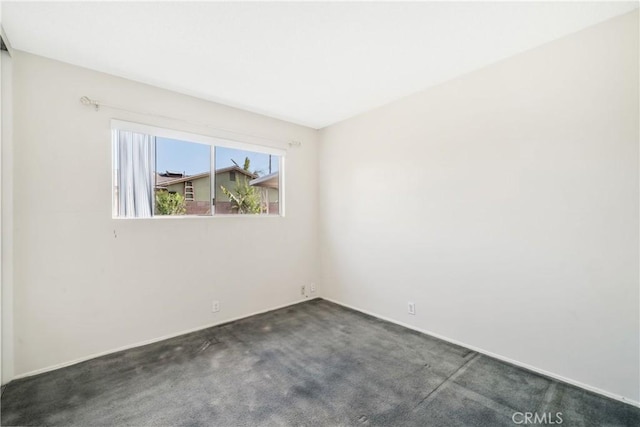 spare room with baseboards and dark carpet