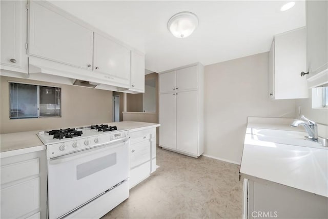 kitchen featuring baseboards, a sink, light countertops, white gas stove, and white cabinetry