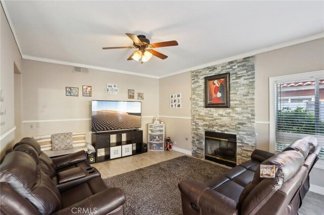 living room featuring baseboards, visible vents, ceiling fan, crown molding, and a stone fireplace