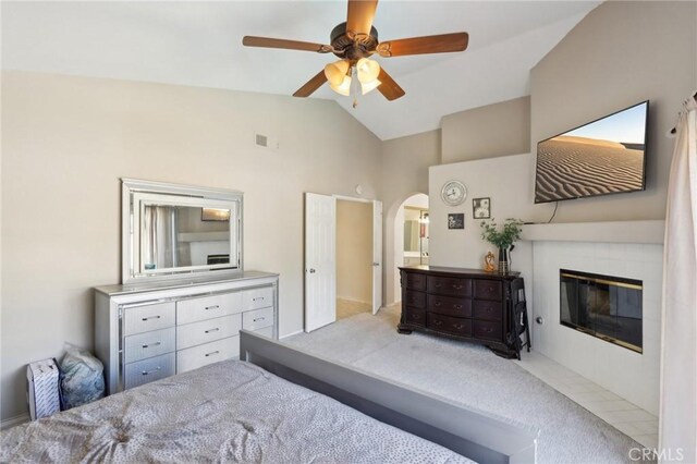 carpeted bedroom with arched walkways, vaulted ceiling, visible vents, a ceiling fan, and a tile fireplace