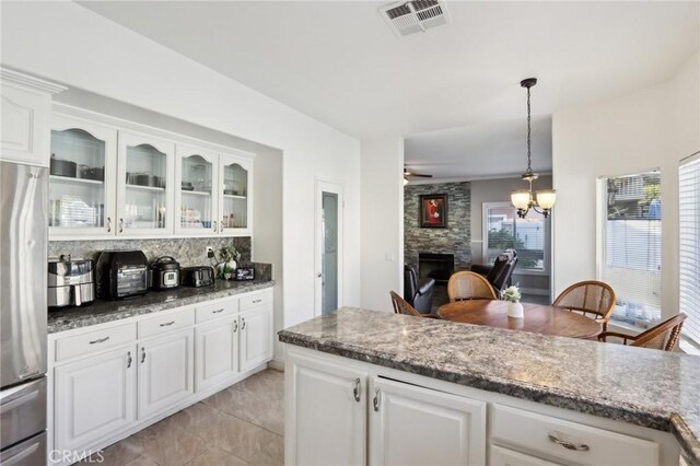 kitchen with white cabinets, stainless steel fridge, tasteful backsplash, visible vents, and glass insert cabinets