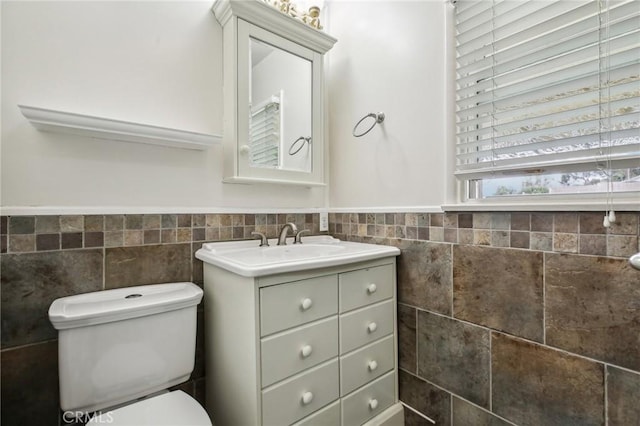 bathroom with vanity, wainscoting, toilet, and tile walls