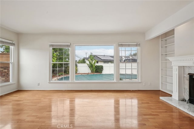 unfurnished living room featuring baseboards, built in shelves, wood finished floors, and a fireplace