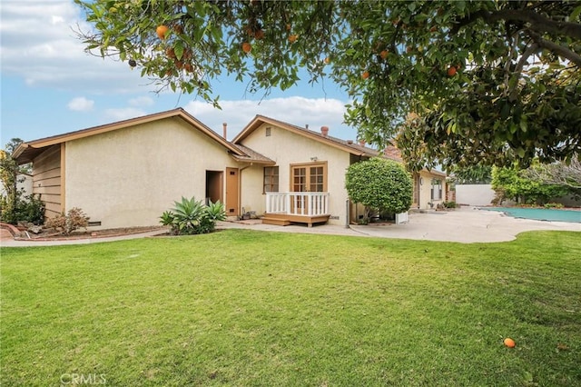 view of front of home with stucco siding, a wooden deck, a patio area, and a front lawn