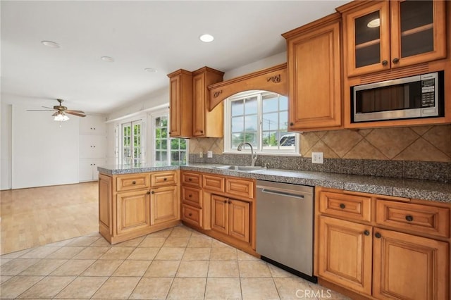 kitchen with appliances with stainless steel finishes, a sink, a peninsula, a ceiling fan, and decorative backsplash