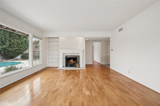 unfurnished living room with a premium fireplace, visible vents, and light wood-type flooring