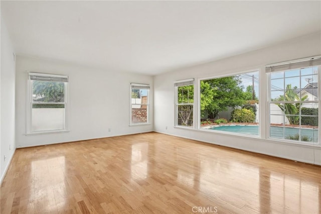 spare room with baseboards, plenty of natural light, and light wood finished floors