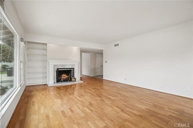 unfurnished living room featuring a high end fireplace, plenty of natural light, light wood finished floors, and visible vents