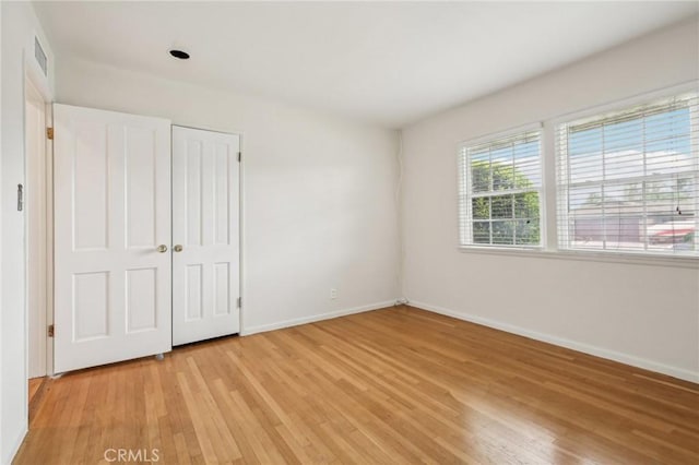 unfurnished bedroom featuring baseboards, visible vents, light wood finished floors, and a closet