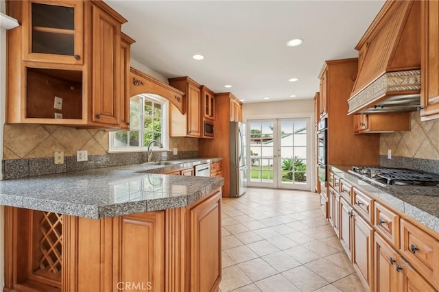 kitchen with tile countertops, appliances with stainless steel finishes, glass insert cabinets, and premium range hood