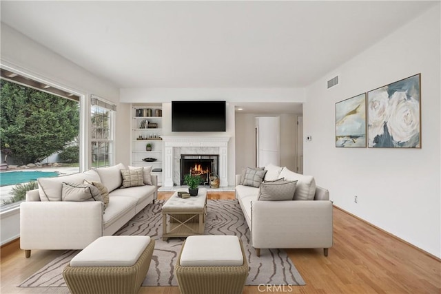 living area with visible vents, built in features, wood finished floors, and a high end fireplace
