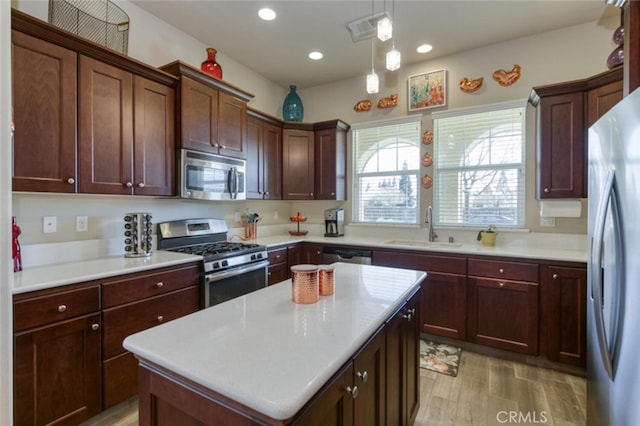 kitchen with a kitchen island, appliances with stainless steel finishes, a sink, light countertops, and decorative light fixtures