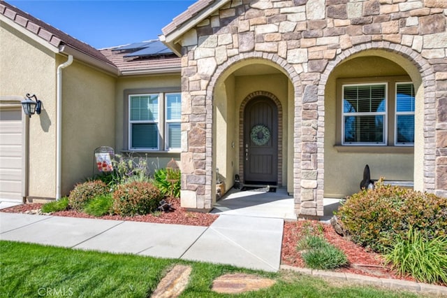 entrance to property with a shingled roof, stucco siding, stone siding, and solar panels
