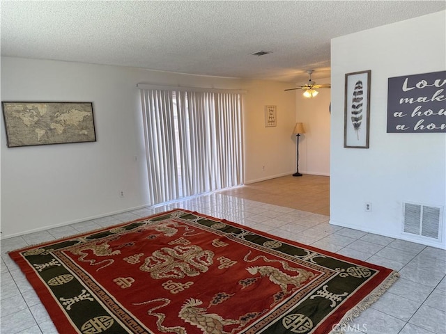 empty room with a textured ceiling, visible vents, tile patterned flooring, and a ceiling fan