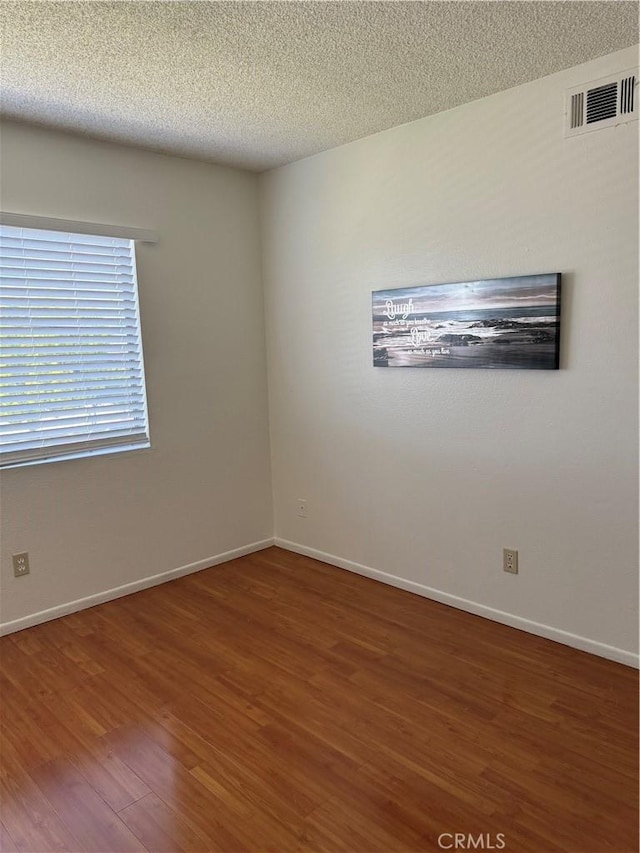 spare room with baseboards, wood finished floors, visible vents, and a textured ceiling
