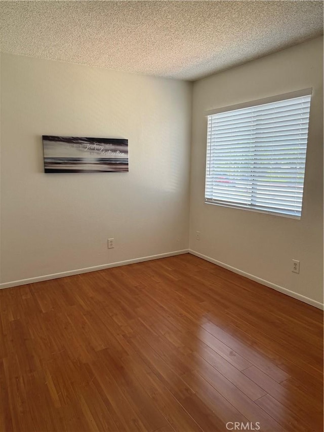 unfurnished room featuring baseboards, wood finished floors, and a textured ceiling