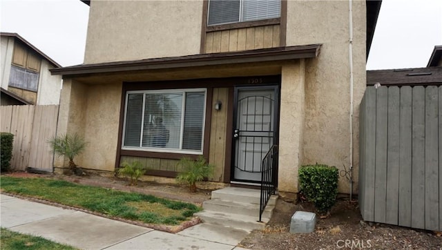 view of exterior entry featuring fence, radiator, and stucco siding