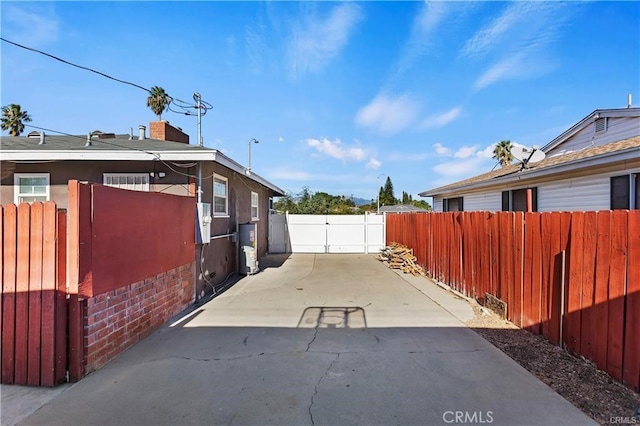 view of property exterior featuring a patio area, fence, brick siding, and a gate