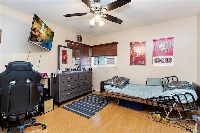 bedroom with ceiling fan, cooling unit, and wood finished floors