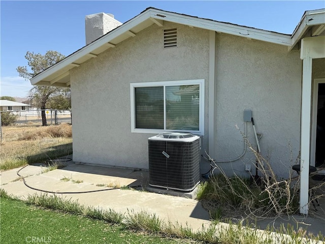 view of side of property featuring fence, stucco siding, central AC unit, and a chimney