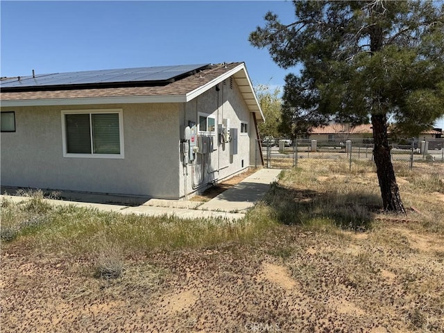 view of side of home featuring fence, stucco siding, and roof mounted solar panels