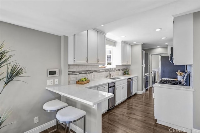 kitchen featuring tasteful backsplash, a sink, appliances with stainless steel finishes, a breakfast bar, and white cabinetry