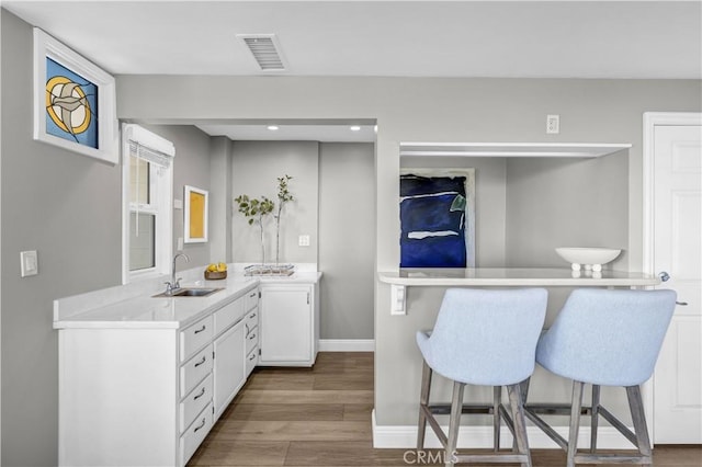 kitchen featuring baseboards, light countertops, white cabinets, visible vents, and a sink