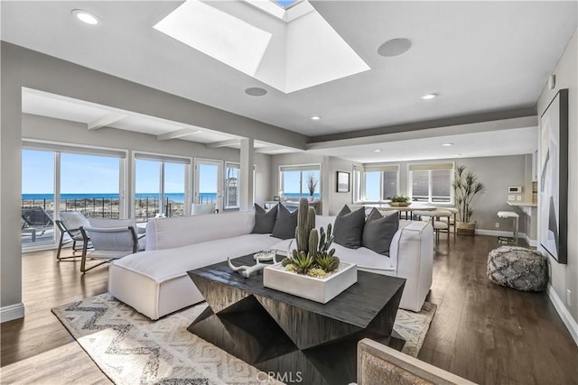 living room featuring a skylight, baseboards, beamed ceiling, and wood finished floors