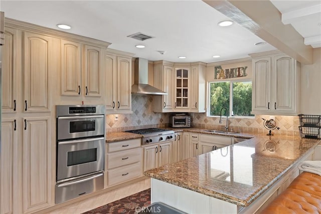 kitchen featuring a sink, stainless steel appliances, a warming drawer, visible vents, and wall chimney range hood