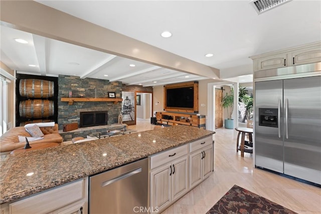 kitchen featuring cream cabinets, dark stone counters, appliances with stainless steel finishes, visible vents, and open floor plan
