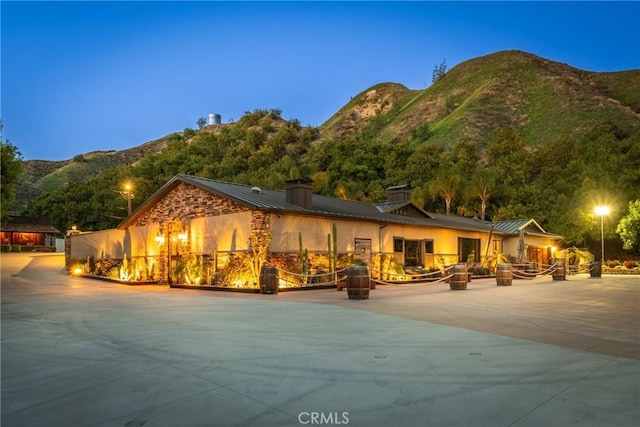 rear view of house featuring stone siding, a chimney, a standing seam roof, metal roof, and a mountain view