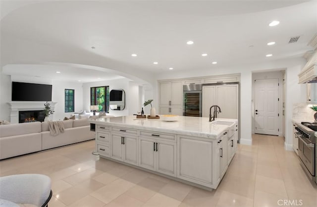 kitchen featuring recessed lighting, arched walkways, open floor plan, and a center island with sink
