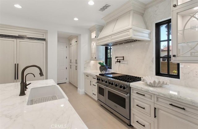 kitchen featuring light stone countertops, a sink, decorative backsplash, high quality appliances, and premium range hood