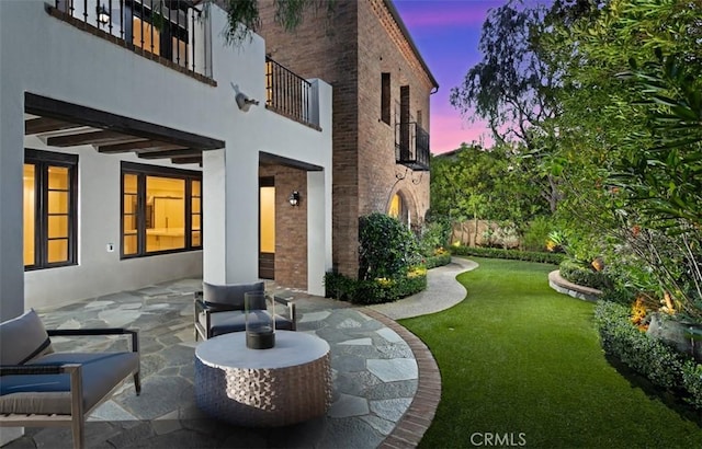 exterior space with stucco siding, brick siding, a patio, a balcony, and a lawn