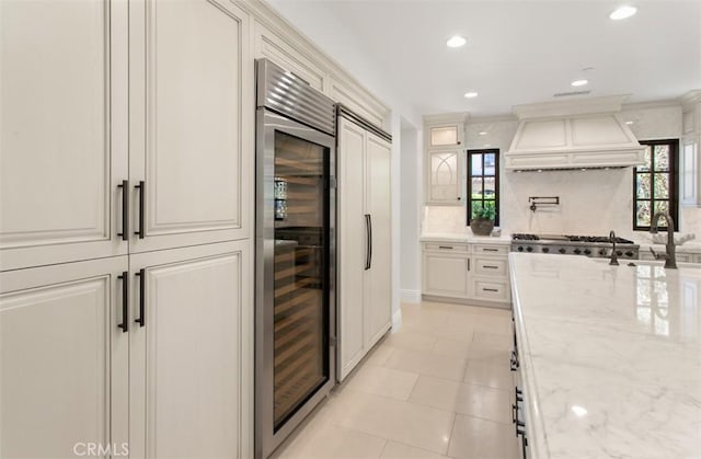 kitchen with beverage cooler, light stone countertops, custom exhaust hood, recessed lighting, and backsplash