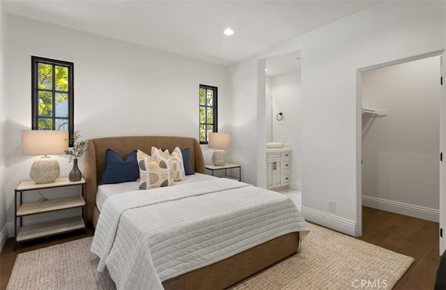 bedroom with baseboards, wood finished floors, a walk in closet, and multiple windows