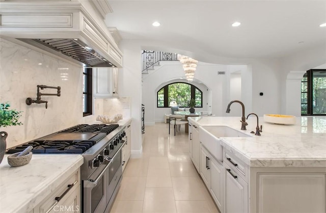kitchen featuring tasteful backsplash, an island with sink, double oven range, custom range hood, and a sink