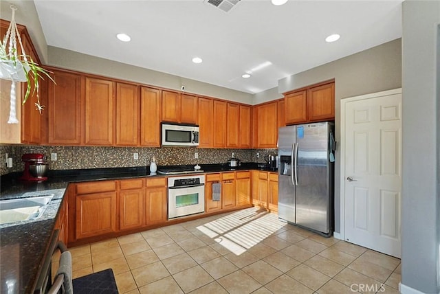 kitchen featuring light tile patterned flooring, visible vents, brown cabinetry, decorative backsplash, and stainless steel appliances