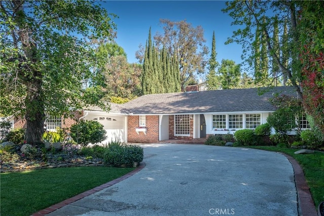 single story home with concrete driveway, a chimney, a front yard, brick siding, and a garage