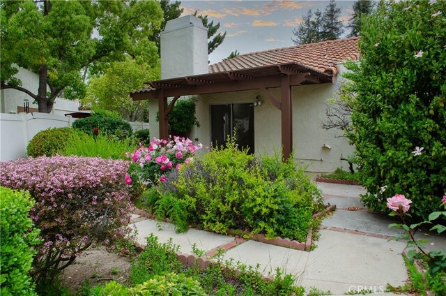 view of side of home featuring a pergola, a tiled roof, a chimney, stucco siding, and fence