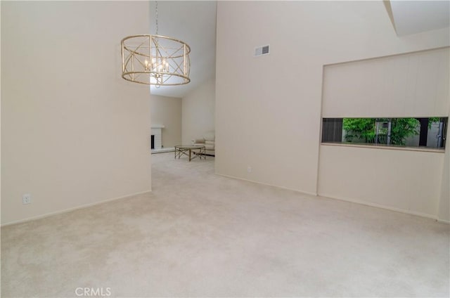 unfurnished room featuring carpet flooring, visible vents, a fireplace with raised hearth, an inviting chandelier, and a high ceiling