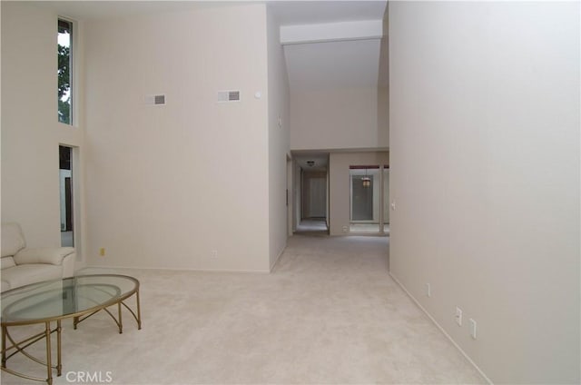 corridor with visible vents, a high ceiling, and carpet flooring