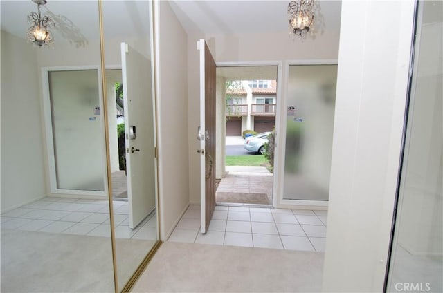 carpeted foyer entrance featuring an inviting chandelier, tile patterned flooring, and baseboards