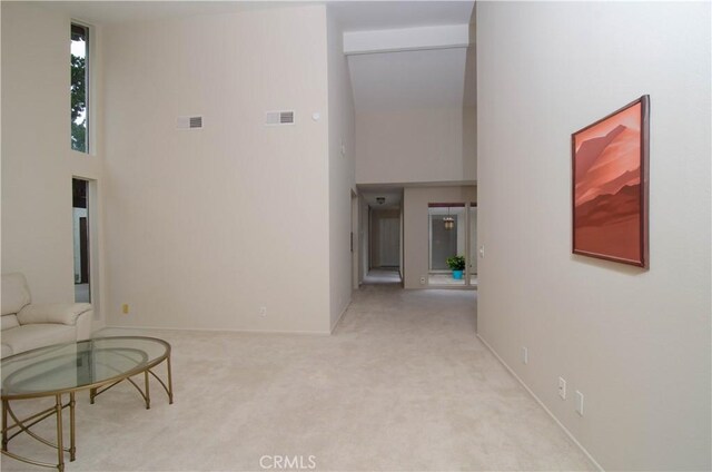 hallway with visible vents, a high ceiling, and carpet floors