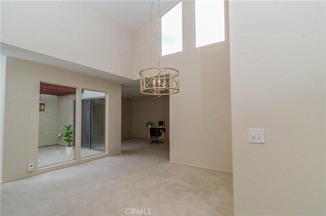 spare room featuring a towering ceiling, a chandelier, carpet flooring, and baseboards