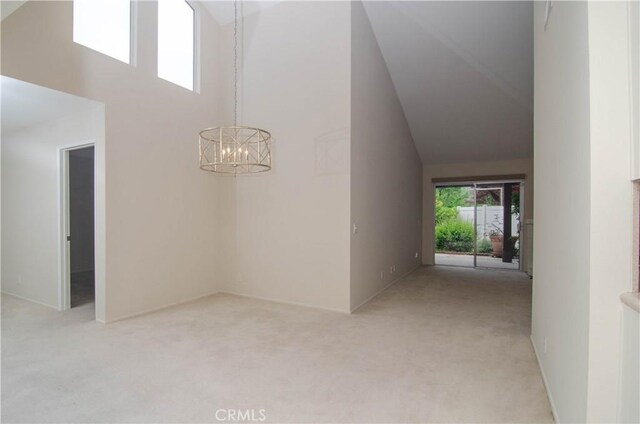 corridor featuring an inviting chandelier, light colored carpet, and a towering ceiling