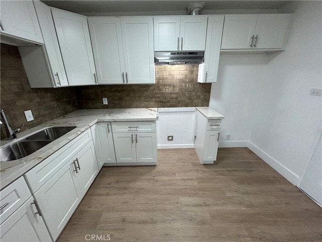 kitchen with white cabinets, light wood-style flooring, a sink, backsplash, and under cabinet range hood