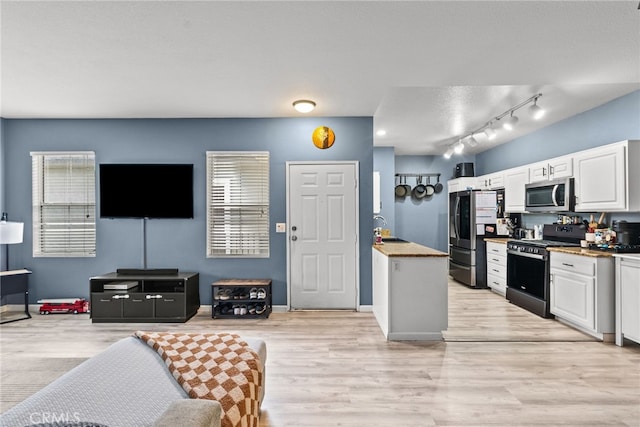 kitchen featuring stainless steel appliances, a sink, white cabinetry, light wood-type flooring, and open floor plan