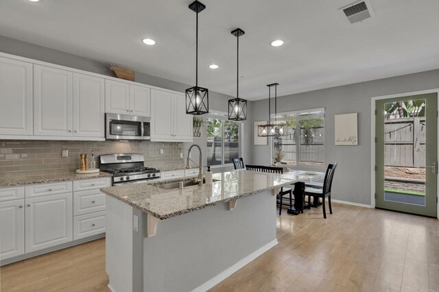 1132 Cherry Tree Ln, Vista, CA 92084 - kitchen featuring appliances with stainless steel finishes, light wood-style flooring, white cabinets, tasteful backsplash, and a center island with sink
